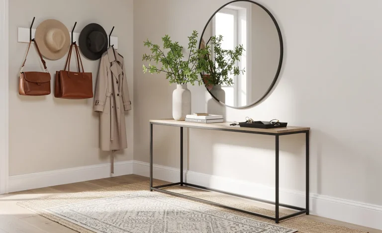 Entrée moderne avec tapis superposés, table console décorée d’un vase de verdure, porte-manteaux avec chapeaux et sacs, et un miroir rond reflétant la lumière naturelle.