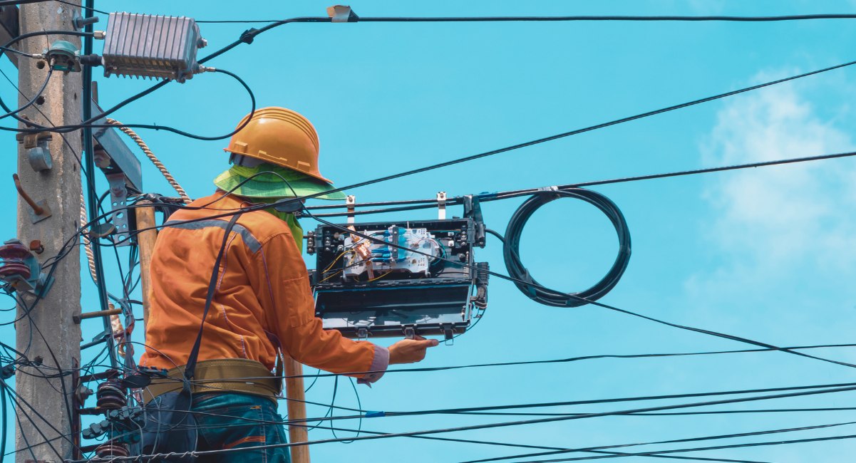 Technicien installant un cable de fibre optique en hauteur sur une echelle en bois