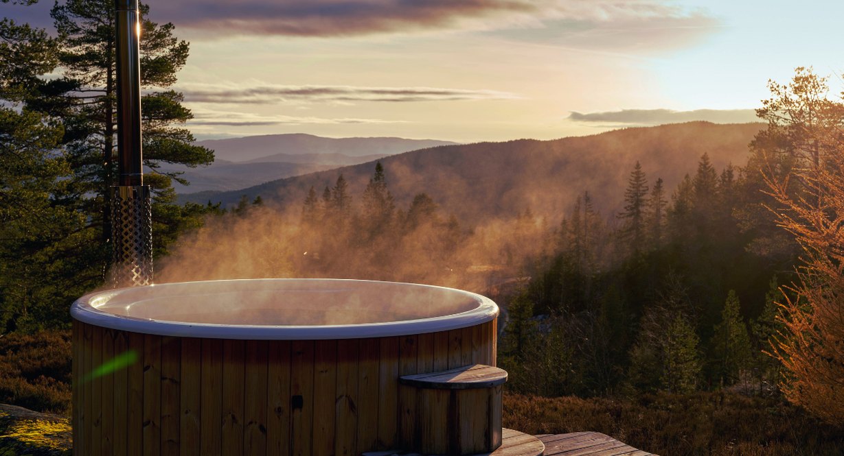 Bain finlandais en bois chauffe au poele, fumant, installe face a une foret de montagne au coucher du soleil