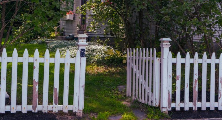 Cloture en bois blanc avec portillon ouvert menant a un jardin fleuri devant une maison