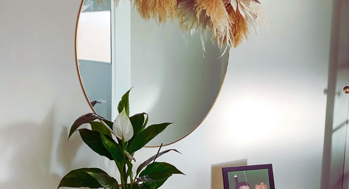 Entrée décorée avec miroir rond, fleurs séchées et plante verte