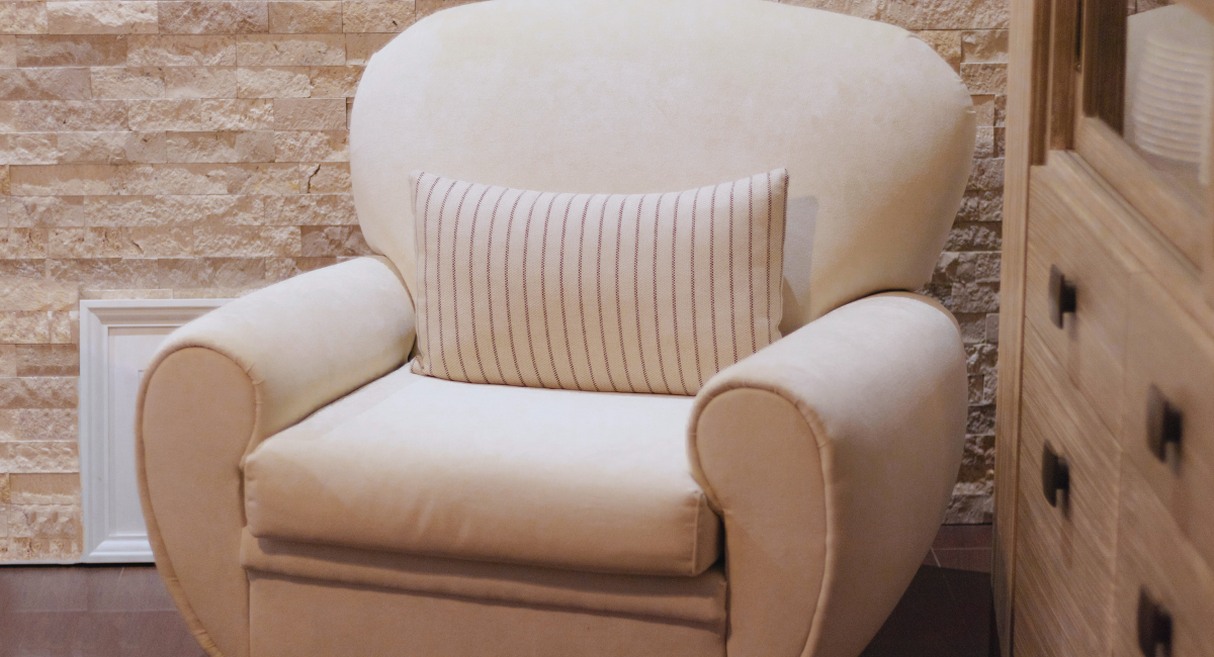 Fauteuil en tissu de couleur écru devant un mur en pierre claire