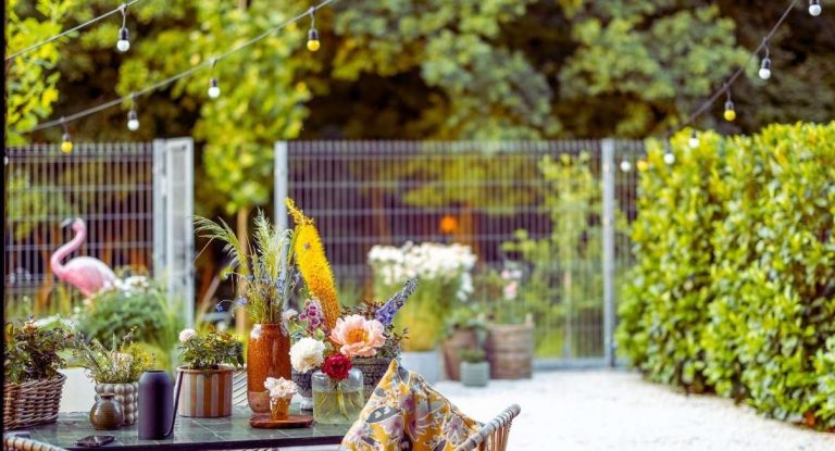 Table de jardin fleurie sous la vegetation avec guirlande lumineuse dans un exterieur ombrage