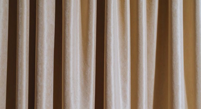 Gros plan sur un tissu de rideau en velours beige aux plis verticaux