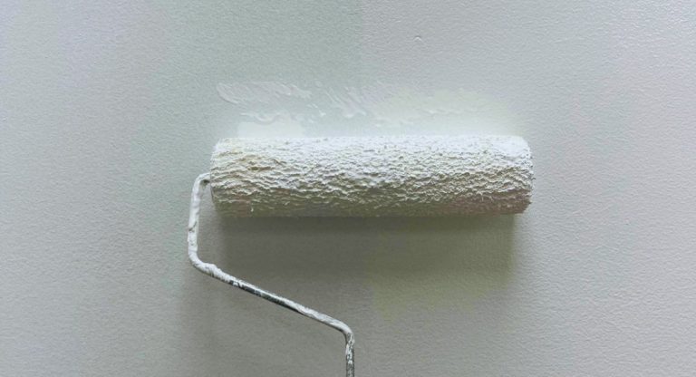 Rouleau appliquant une couche de peinture blanche sur un mur