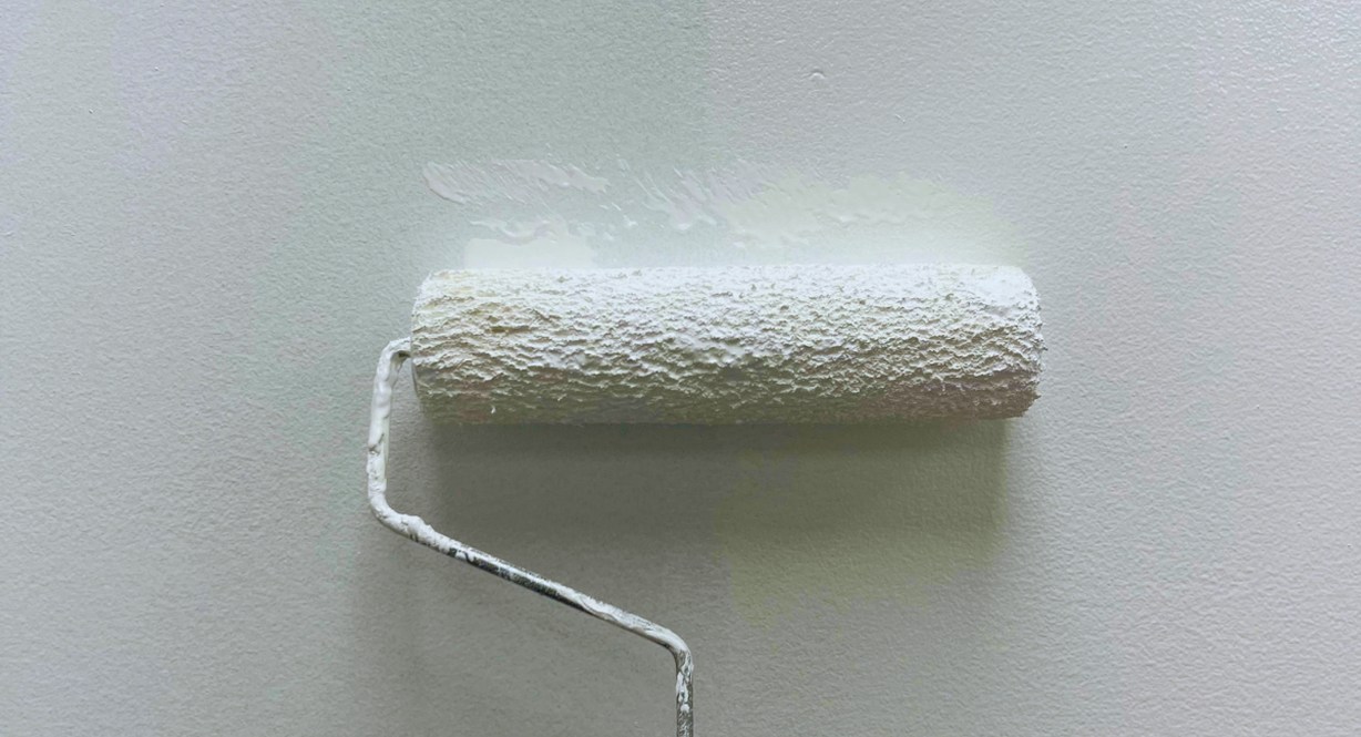 Rouleau appliquant une couche de peinture blanche sur un mur