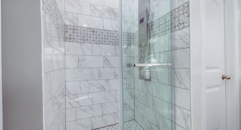 Douche fermée par une paroi en verre transparent, murs en faïence blanche effet marbre et colonne de douche