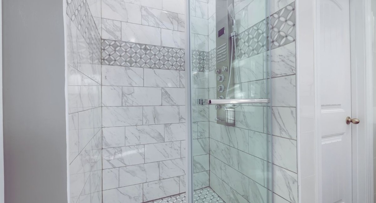 Douche fermée par une paroi en verre transparent, murs en faïence blanche effet marbre et colonne de douche