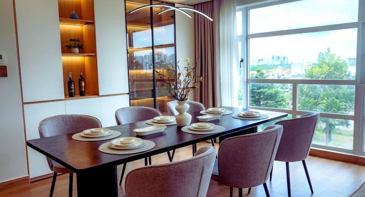 Table à manger rectangulaire en bois foncé dressée avec chaises en tissu devant une baie vitrée