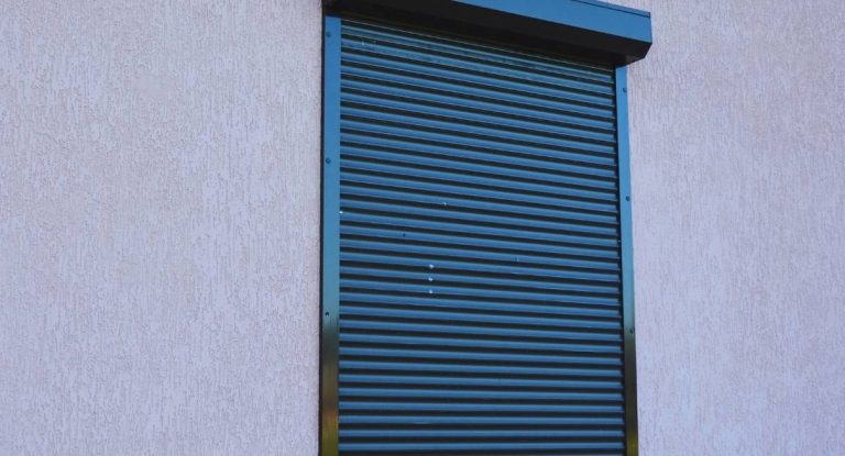 Volet roulant en aluminium fermé devant une fenêtre sur une façade crépie