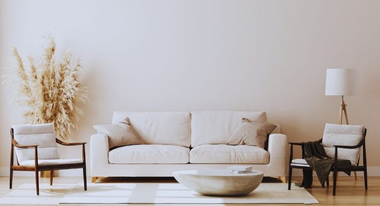 Canapé en tissu beige avec coussins, deux fauteuils en bois et table basse ronde dans un salon clair