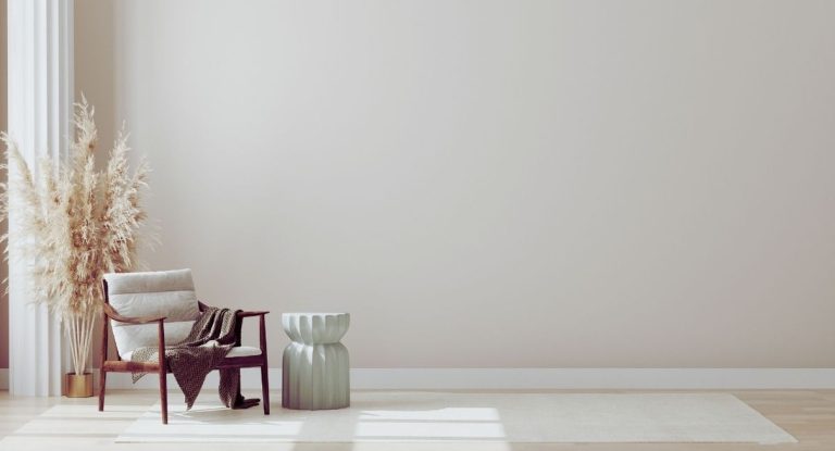 Salon minimaliste aux murs clairs avec un fauteuil en bois, un tabouret vert sauge et un bouquet d'herbes de la pampa