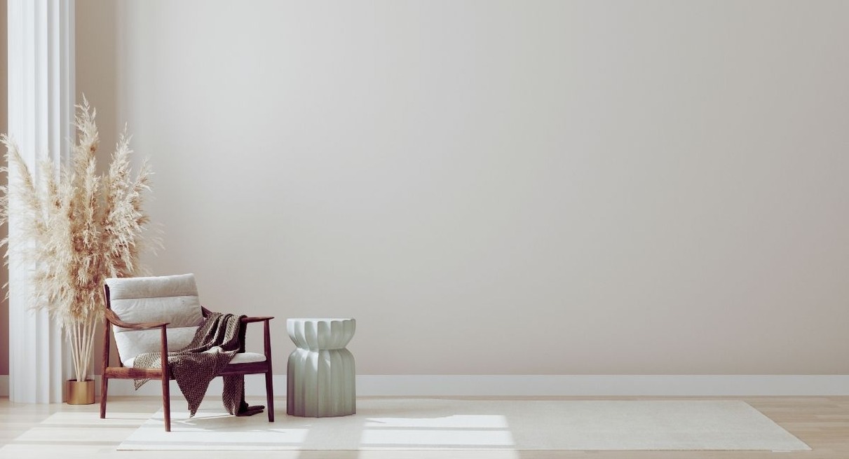 Salon minimaliste aux murs clairs avec un fauteuil en bois, un tabouret vert sauge et un bouquet d'herbes de la pampa